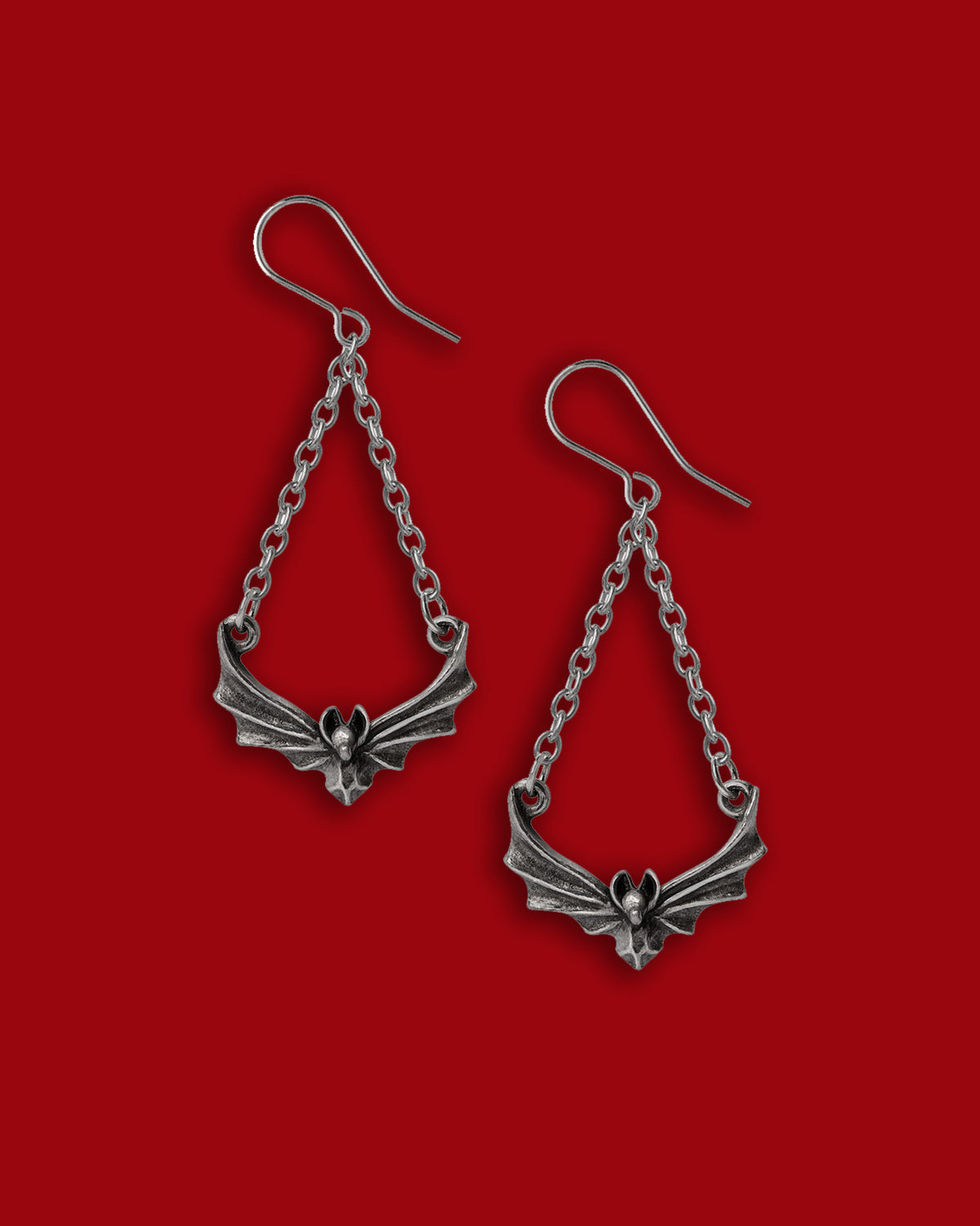 A dramatic pair of gothic‑inspired earrings crafted in antiqued fine English pewter, showcasing stylised bat‑wing motifs suspended from delicate chains that add movement and edge to the design. These statement earrings deliver dark‑romantic flair while remaining comfortably wearable—ideal for nightly outings or bold daytime styling—and embody the mysterious allure of nocturnal elegance with high‑quality metalwork and a refined finish.