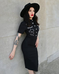 A striking black Barbara Dress crafted from high-stretch Bengaline fabric that contours the body with a structured yet flexible fit. The design features intricate custom barbed wire embroidery running across the bodice, paired with subtle piped western yoke detailing that adds dimension and shape. Decorative silver snap buttons line the front for a vintage-inspired finish, while a hidden back zipper ensures effortless wear and a smooth silhouette.