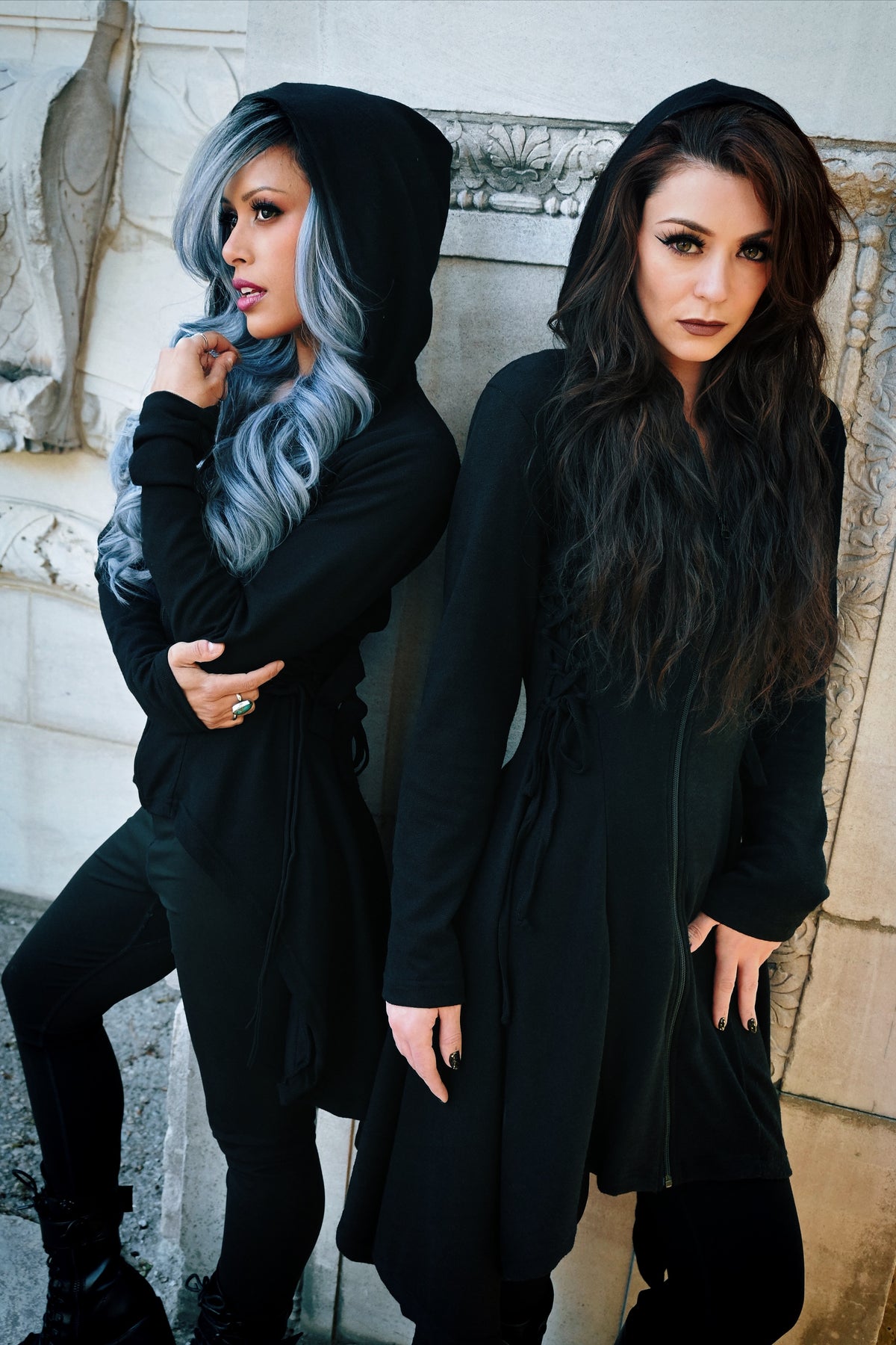 Black zip-up hoodie from Heartless with a soft 100% polyester construction, corset-style side lacing, adjustable back ties, high-low hem, and thumbholes, offering a fitted silhouette, oversized hood, and versatile layering option for casual or statement outfits.