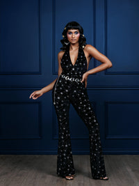 Elegant black velvet Cosmo Jumpsuit adorned with silver starburst embellishments, featuring a low-cut halter neck and form-flattering stretchy fabric, ideal for women seeking a stylish, retro 70s-inspired look for holiday celebrations.