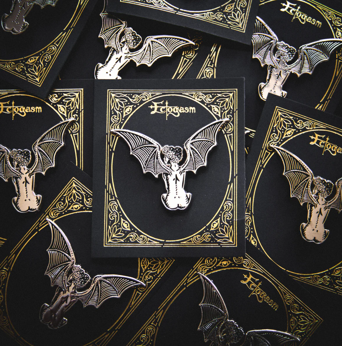 Ectogasm gothic lapel pin in silver metal and black enamel, showcasing a crowned woman with bat wings and celestial hair. Size 2 x 1.5 inches with dual metal clasps for stability. A hauntingly beautiful accessory perfect for leather jackets, purses, or hats, designed and copyrighted by Ectogasm in 2022.
