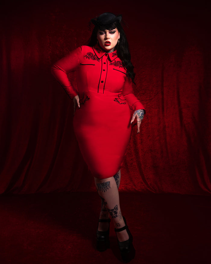 The June Dress in red by Katakomb is a stunning dark western-inspired stretch bengaline dress featuring detailed rose and thorn embroidery on the collar, cuffs, bust, and hips. Designed with pleather piping and long piped sleeves with faux snap cuffs, this elegant red dress combines gothic romance and vintage rockabilly charm for a bold, statement-making outfit.