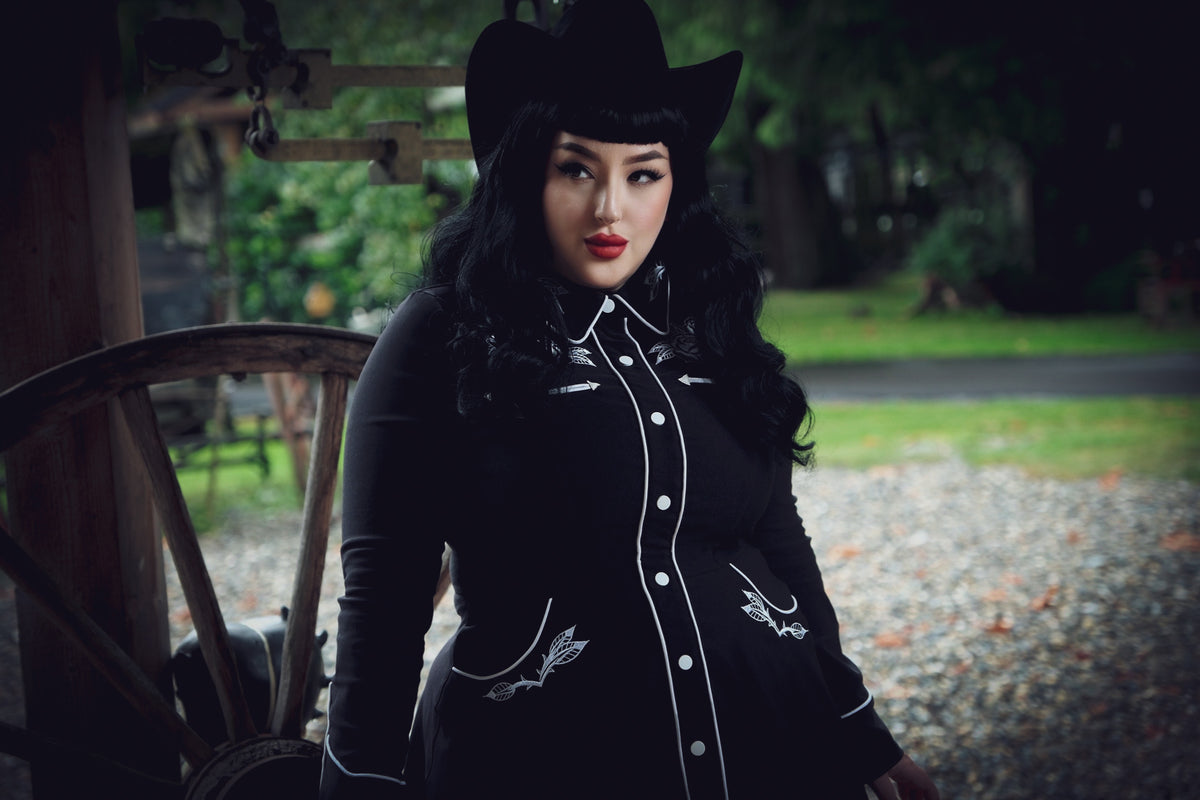 June Dress in black and white with a flattering skater skirt cut, intricately embroidered roses and thorns across the collar, cuffs, bust, and hips, subtle white piping along the seams, long piped sleeves with faux snap cuffs, and functional deep pockets, designed for women seeking both elegance and practicality in one versatile dress.