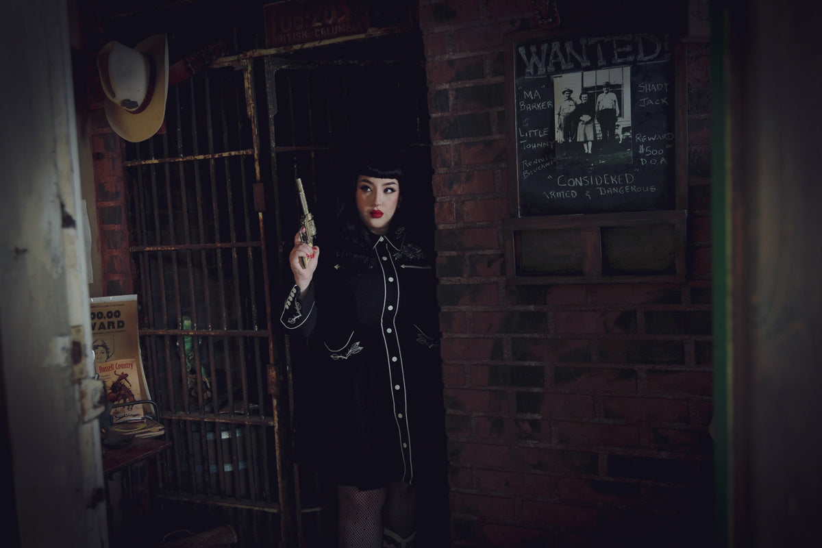 Women’s black and white skater dress featuring a playful flared skirt with deep pockets, long piped sleeves with faux snap cuffs, detailed rose and thorn embroidery on the collar, bust, hips, and cuffs, and white piping accents, combining timeless feminine style with functional design for day-to-night wear.