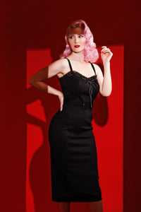 The dress in luxurious black is a bold and elegant piece crafted from a heavy-weight poly blend designed by Jessica Louise. This figure-flattering dress features a sweetheart neckline with delicate ruffled details and a charming ribbon bow at the bust, enhancing its sultry yet feminine appeal. Designed for both comfort and confidence, the dress includes enhanced cup sizing, adjustable shoulder straps, and a ruched back panel for easy wear. Its high-stretch fabric contours beautifully to your curves.