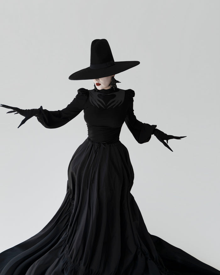 Phantom Blouse in black, made from high-stretch polyester, showcasing a sheer mesh chest cut-out with Naya’s intricate hand motif, puffed shoulders, and long gathered sleeves that add old-world gothic elegance and versatile styling options.
