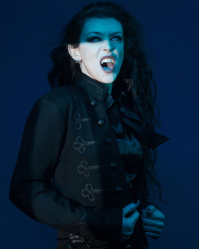 A gothic-inspired cropped military jacket crafted from structured stretch ponte fabric, featuring ornate braided trim along the front and sleeves, antique-style embossed ouroboros buttons, and a high mandarin collar. This tailored black jacket combines Victorian elegance with modern edge, offering a fitted yet comfortable silhouette perfect for layering over dresses, corsets, or slim tops.