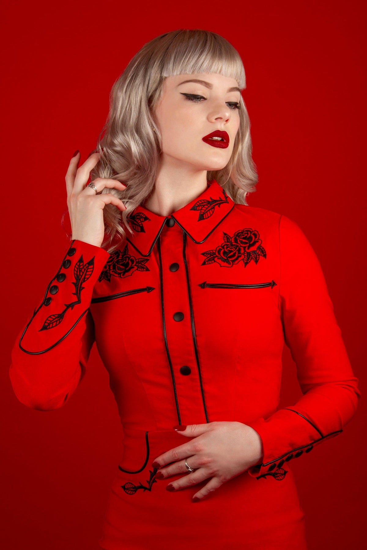 A darkly romantic red dress designed by Katakomb, the June Dress is made from high-quality stretch bengaline fabric that enhances comfort and shape. Featuring embroidery of roses and thorns on key areas, piped detailing, and faux snap cuffs, it delivers a vintage western-inspired look with modern gothic elegance.