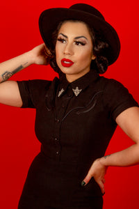 This sophisticated black Wanda Pencil Dress exudes confidence and timeless beauty with its sleek silhouette, crafted from comfortable, stretchy Bengaline for a perfect fit. The design includes faux front snaps, a hidden back zipper for ease of wear, and luxurious pleather piping for added texture. Two removable silver collar clips complete the look, making it an ideal piece for both professional and evening settings.