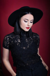 A retro styled model posing frontwards while sporting a black, wide brim American Gothic hat.