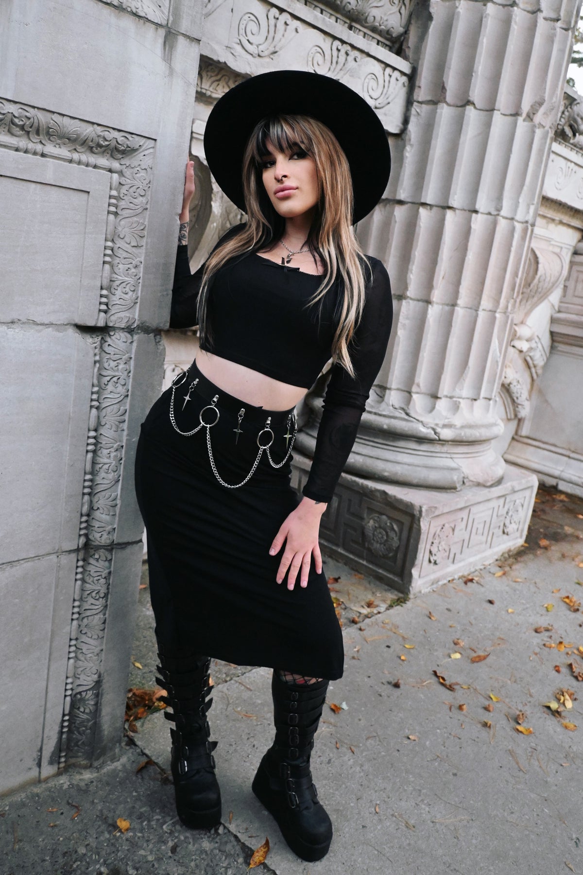 A black faux leather belt adorned with large silver-tone rings, hanging chains, and dagger charms, creating a striking gothic-inspired look. The adjustable back buckle ensures a secure and comfortable fit, making it an edgy accessory for skirts, dresses, or trousers that instantly adds attitude and style.
