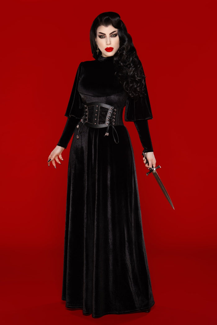 Model posing against red background wearing Arcadia Dress with a black belt and holding a dagger