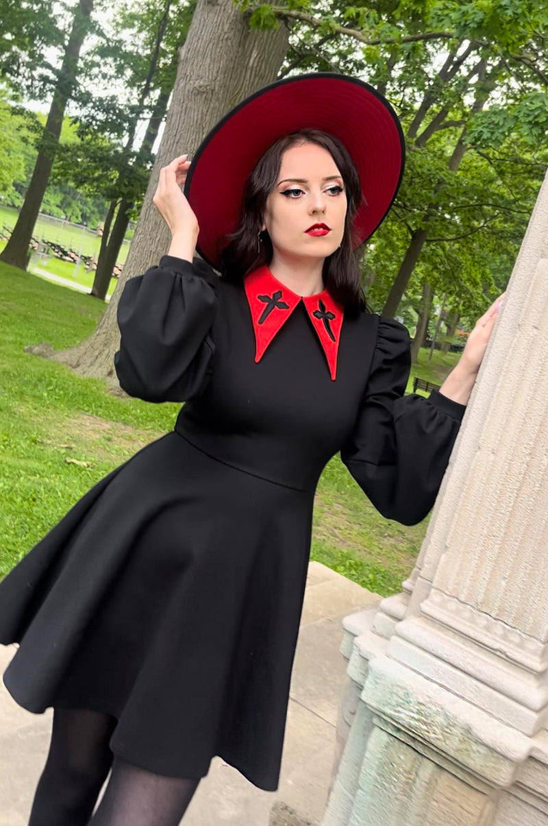 This charming black Baptism Dress captures a moonlight-inspired elegance, with a striking pointed collar that features subtle cross embroidery. The dress offers a choice of a solid black collar for classic sophistication or a red collar for a playful accent. Puff shoulders and flowing bishop sleeves add a touch of drama and style, while the high-stretch ponte fabric provides warmth, comfort, and durability for special occasions.
