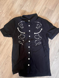 A distinctive black men’s short-sleeve shirt that merges western toughness with gothic flair, featuring custom barbed wire and arrow embroidery spanning the chest for a powerful visual impact. The Bengaline material ensures flexibility, structure, and long-lasting shape retention, while the matte snap buttons reinforce the shirt’s rugged character. Designed for men who appreciate detailed craftsmanship and alternative fashion aesthetics, this piece offers comfort, durability, and unmistakable style.