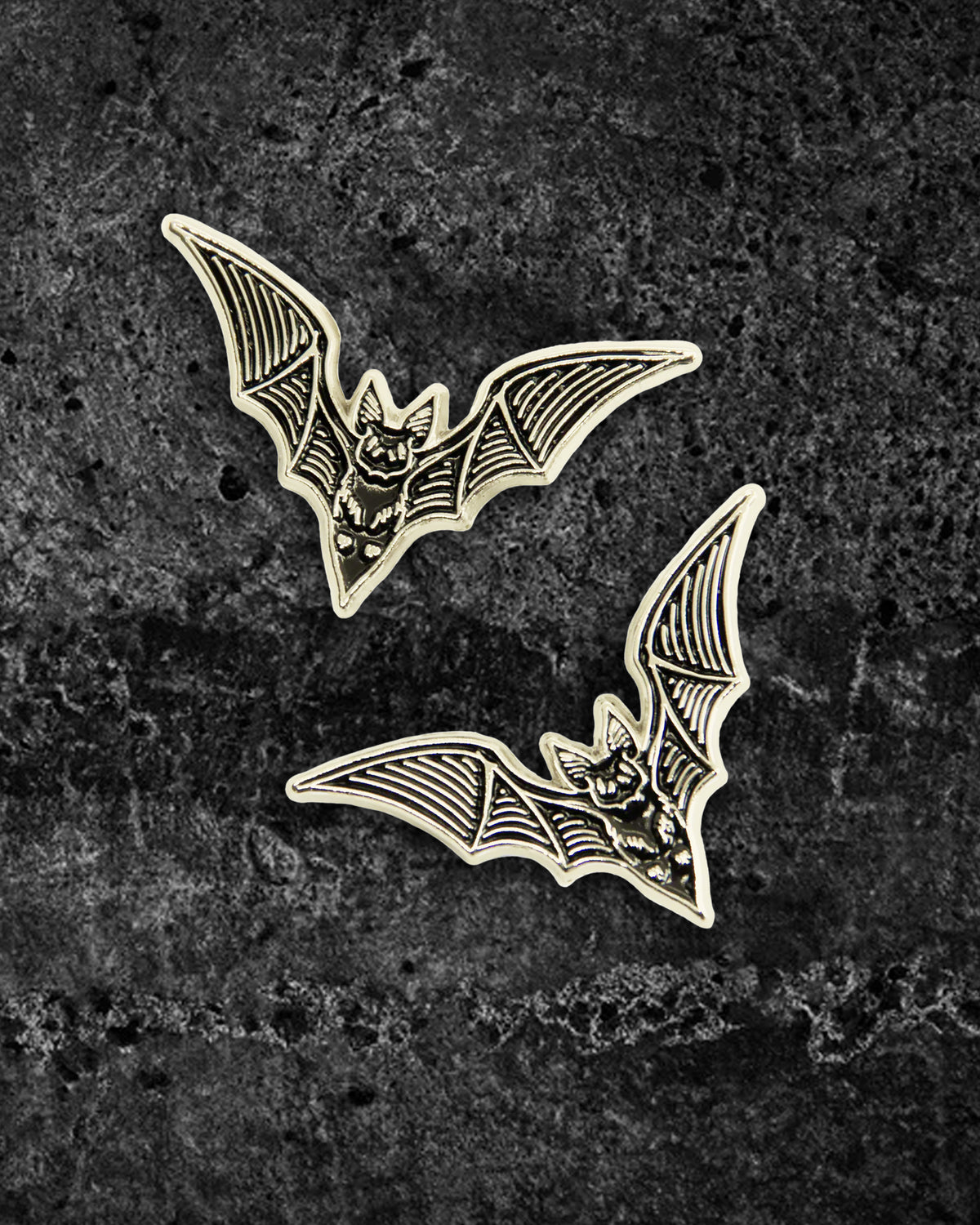 Pair of silver and black enamel bat pins by Ectogasm, featuring fine etching detail in the brand’s signature style. Each pin measures 1.3 x 0.8 inches with dual metal tie tacks to prevent spinning, perfect for adding spooky flair to collar points, jackets, shirts, or layered with other dark fashion pins.
