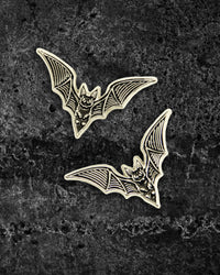 Pair of silver and black enamel bat pins by Ectogasm, featuring fine etching detail in the brand’s signature style. Each pin measures 1.3 x 0.8 inches with dual metal tie tacks to prevent spinning, perfect for adding spooky flair to collar points, jackets, shirts, or layered with other dark fashion pins.