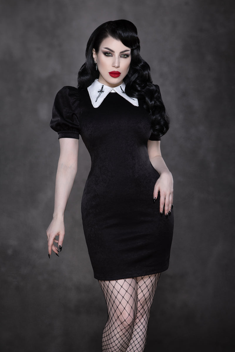 The Bellatrix Dress showcases a sleek, figure-hugging black suede body with dramatic puff sleeves and an exaggerated oversized white collar adorned with black sword embroidery, delivering a striking vintage gothic aesthetic that blends retro 60s style with contemporary alternative fashion trends, ideal for bold, statement outfits.