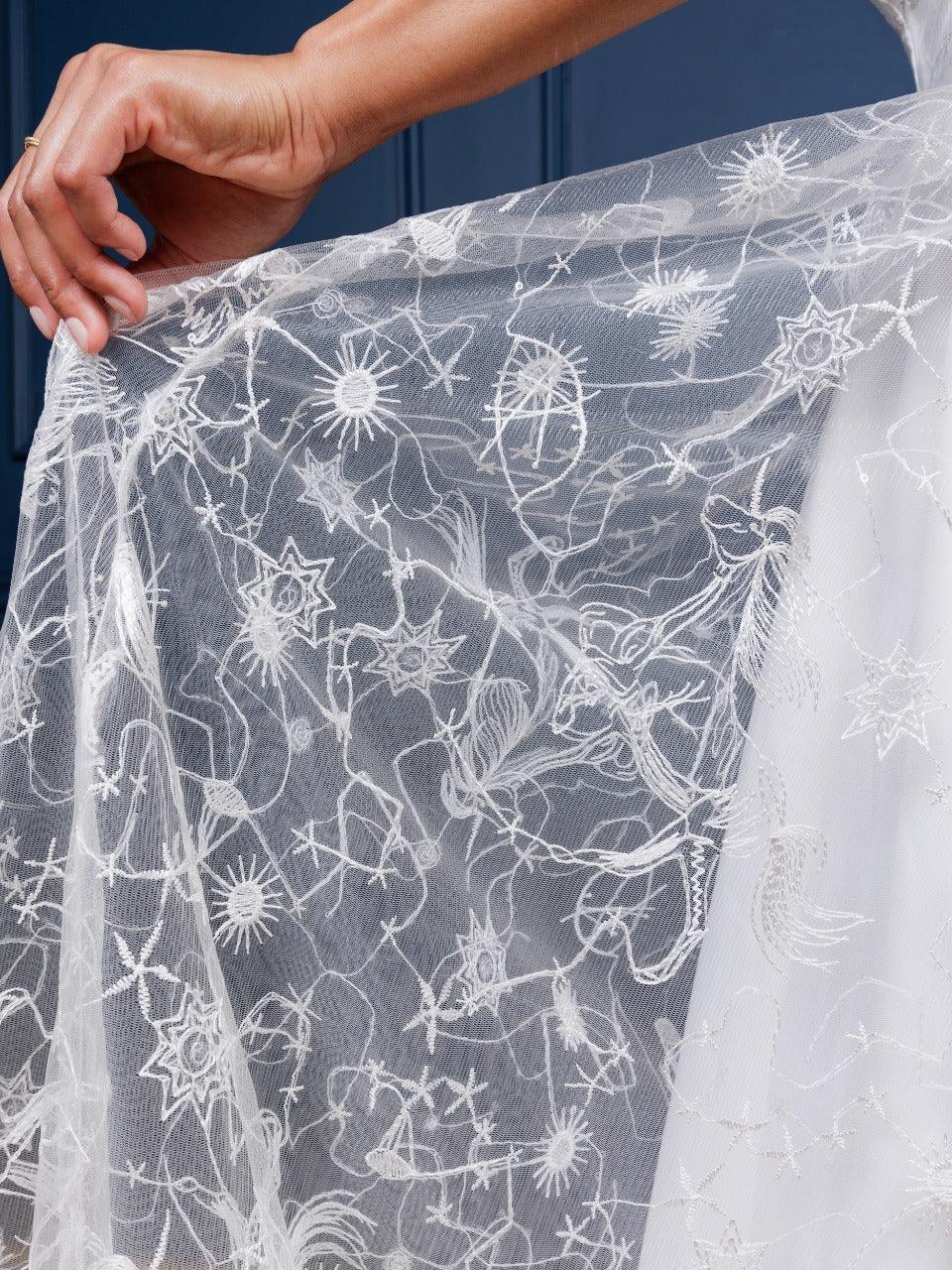 Sophisticated Celestial Dress in black or white embroidered chiffon, featuring a subtle starry constellation print, sparkly shimmer, low-cut neckline, and cross-strap accents. Perfect for special occasions, evening celebrations, or formal gatherings, this maxi dress combines modern chic with timeless elegance.