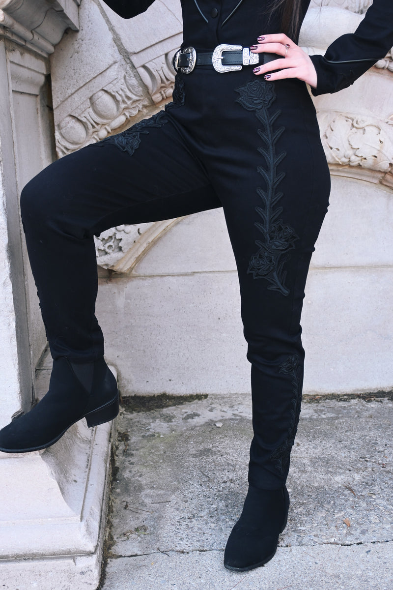Black stretch denim Dallas Pants, high-waisted and form-fitting, designed with tonal black rose and thorn embroidery along both legs. Includes functional belt loops and a back zipper closure, combining edgy, dark romantic style with comfortable, structured wear.
