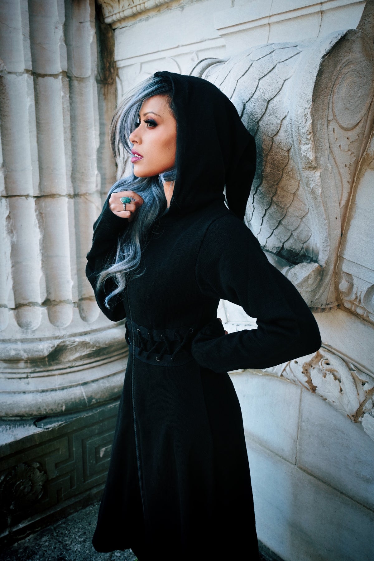 A gothic-inspired, full-length black cardigan with a fitted, laced bodice and structured edges, made of 100% polyacrylic, featuring a front zip closure, oversized hood, high-low hem for dramatic flow, and thumbholes, ideal for creating moody, layered alternative fashion ensembles.