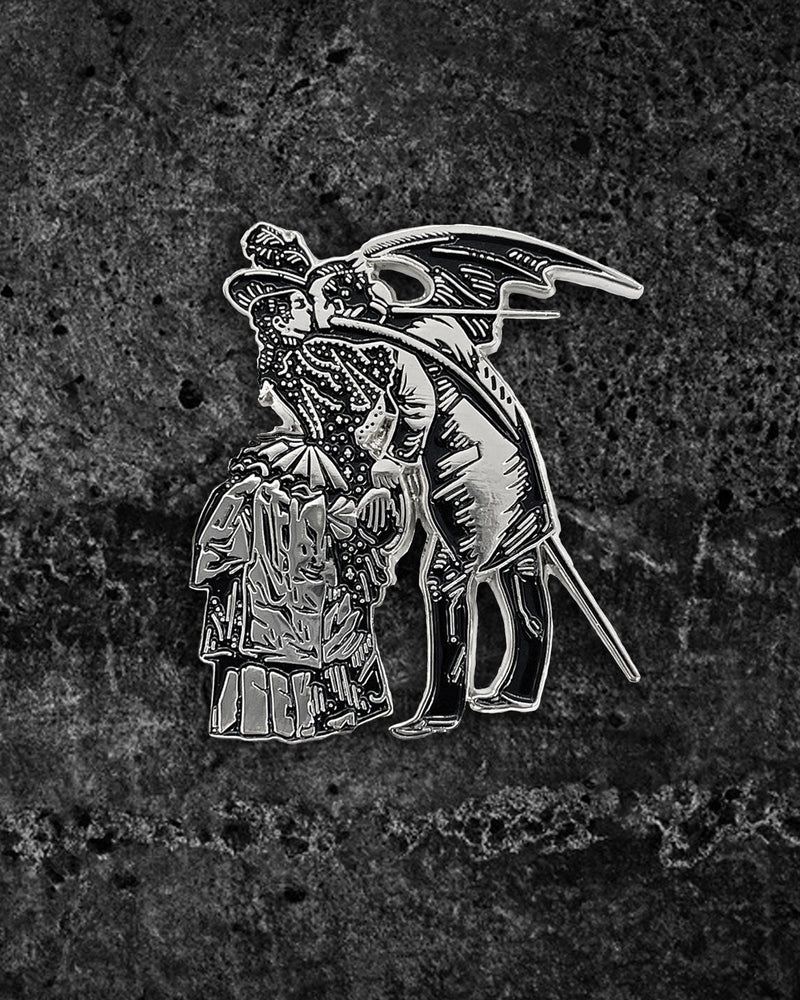 Large silver and black enamel gothic pin inspired by Max Ernst’s surrealist collage from Une Semaine De Bonté, featuring a Victorian-dressed woman kissing a winged man with devilish wings. Measures 2 x 1.71 inches with dual metal clasps to prevent spinning, perfect for jackets, backpacks, or alternative unisex fashion sets.