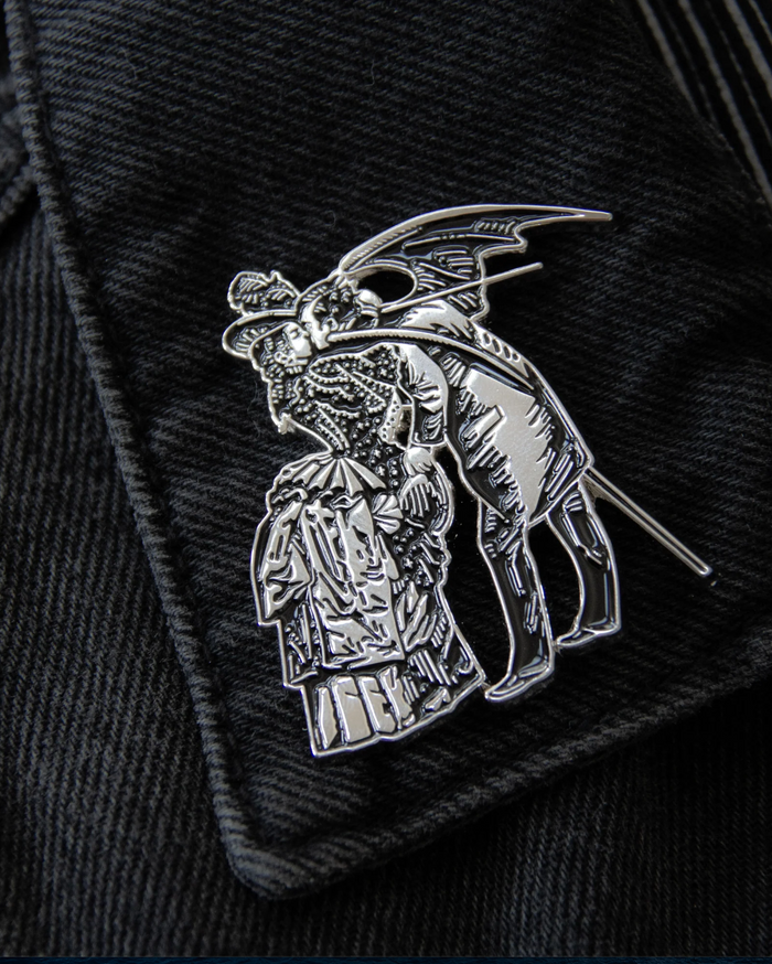 Silver metal and black enamel enamel brooch inspired by Gustave Doré and Max Ernst, showing a gothic, surreal scene of a woman and a winged man. Size 2 x 1.71 inches with secure dual clasps, ideal for black denim jackets, bags, or layered with other gothic pins for alternative style collections.