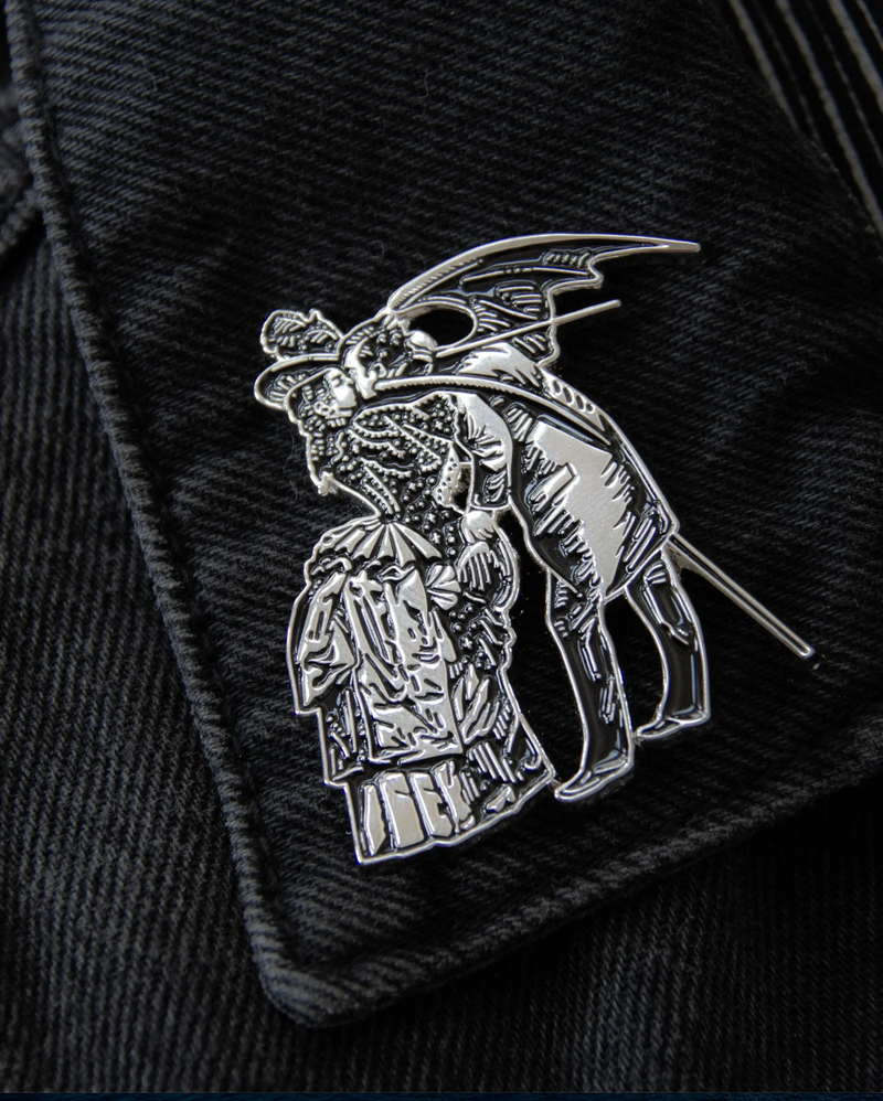 Silver metal and black enamel enamel brooch inspired by Gustave Doré and Max Ernst, showing a gothic, surreal scene of a woman and a winged man. Size 2 x 1.71 inches with secure dual clasps, ideal for black denim jackets, bags, or layered with other gothic pins for alternative style collections.