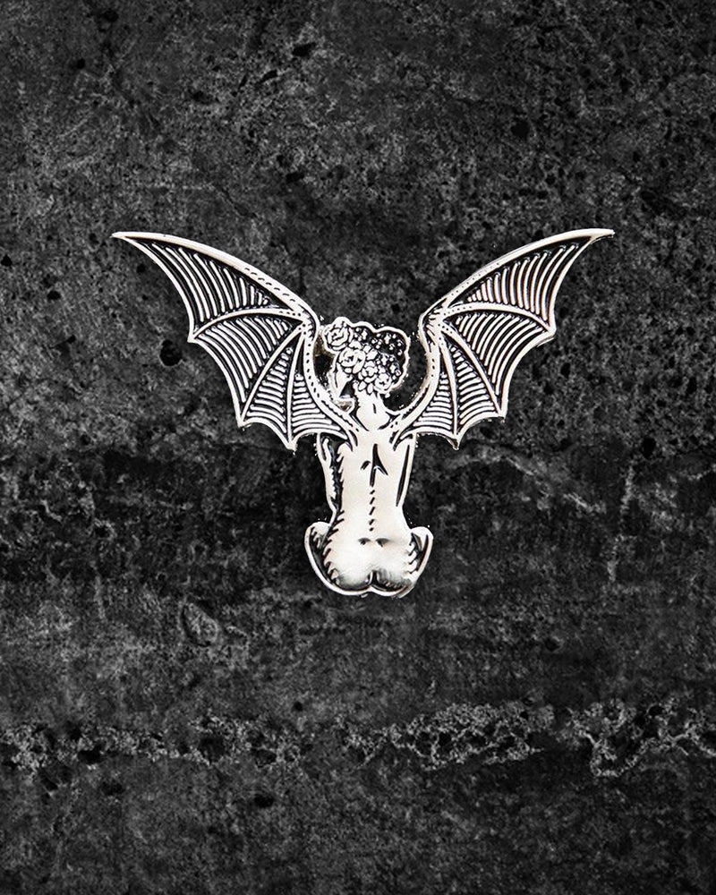 Silver and black enamel lapel pin featuring a nude woman with large outstretched bat wings and a crown of roses in her black, star-filled hair. Measuring approximately 2 x 1.5 inches, this eerie yet elegant gothic pin by Ectogasm includes two metal clasps for secure wear on jackets, hats, or bags.