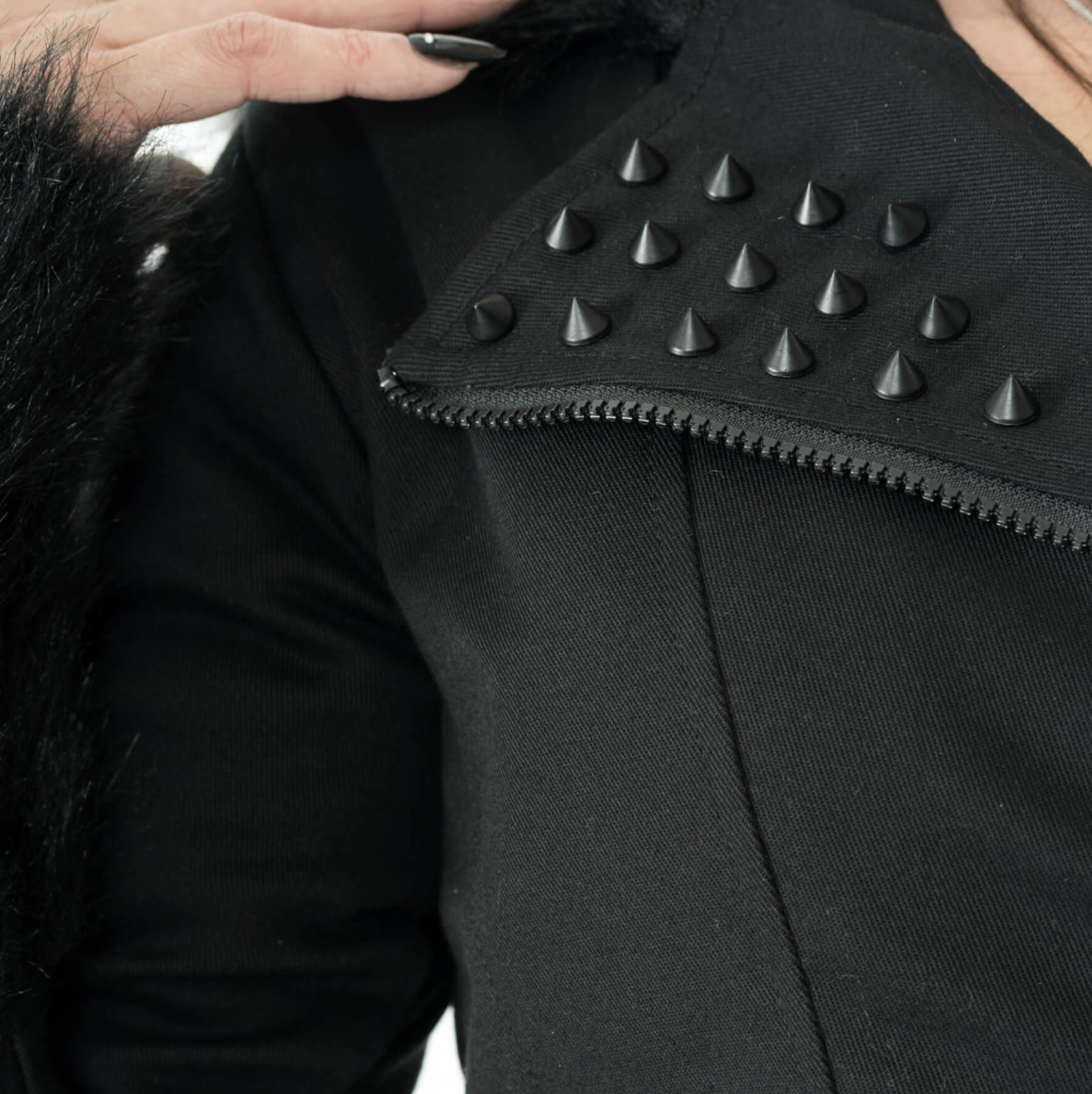 Black Effia Jacket by Heartless combining edgy design and practicality with durable cotton blend outer, polyester faux fur lining, spike studs, asymmetrical zipper, panel seaming, plush hood and cuffs, and adjustable side straps for a fitted and stylish cold-weather jacket.