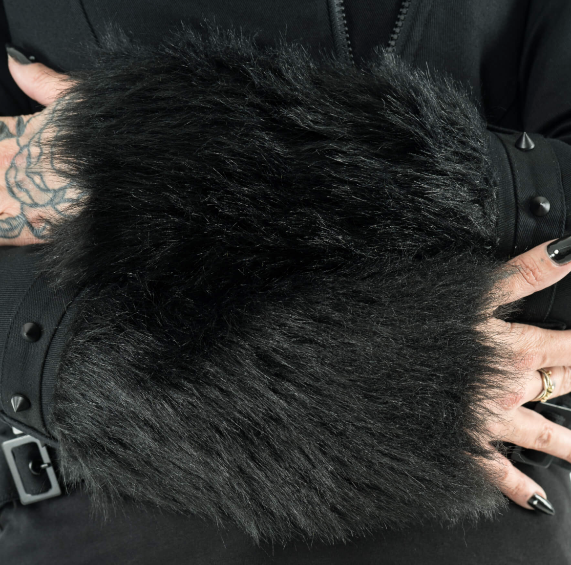 Effia Jacket in black, designed by Heartless with structured cotton fabric, soft polyester lining, faux fur hood and cuffs, matte black stud accents, asymmetrical zip closure, panel seaming, and adjustable side straps for a contemporary, warm, and bold outerwear statement.