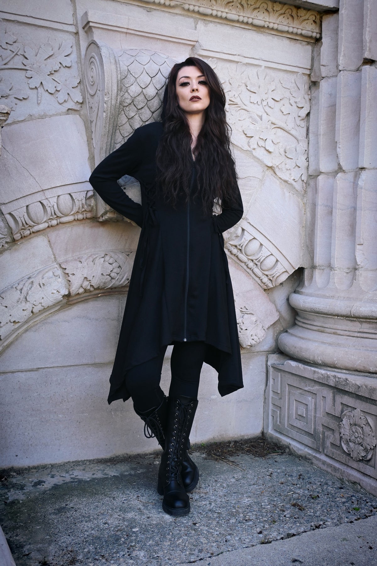 Gothic-inspired Emerson Cardigan by Innocent Lifestyle, made from 100% black polyester, showcasing a soft drape, mid-length cut, zip-up front, side and back corset lacing, elongated hood, and asymmetrical handkerchief hem for versatile styling.