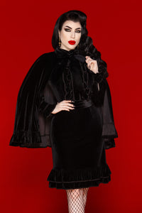 A luxurious one-size black velvet cape designed for elegance and comfort, featuring a soft stretch fabric that drapes effortlessly over any outfit. The cape includes a velvet ribbon tie closure for a secure yet stylish fit, with a ruffled edge adding dramatic flair. Perfect for layering, this versatile cape enhances gothic, elegant, or evening ensembles .