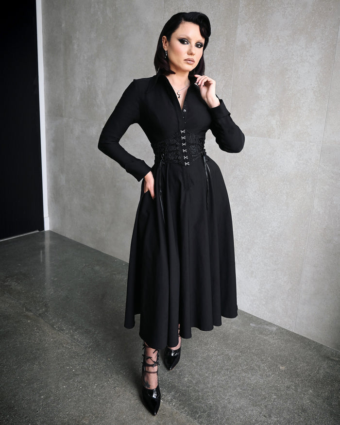 The Homemaker Swing Dress in black is a sophisticated midi-length garment crafted from high-stretch Bengaline fabric, offering both structure and comfort. Its long sleeves and hidden front button placket enhance its classic tailoring, while the functional side pockets add practicality. The flared skirt creates a dramatic silhouette that moves beautifully with every step, embodying Gothic romance.