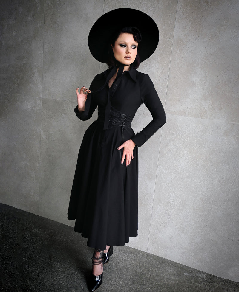 The Homemaker Swing Dress in black is a versatile addition to any wardrobe. Its midi-length design and long sleeves make it suitable for various occasions. The high-stretch Bengaline fabric ensures a comfortable fit, while the hidden front button placket and functional side pockets add functional details. The flared skirt creates a dramatic silhouette, embodying Gothic romance and timeless elegance.
