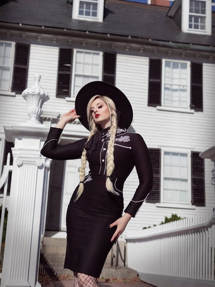 Woman in a black dress with white accents standing in front of a white house.