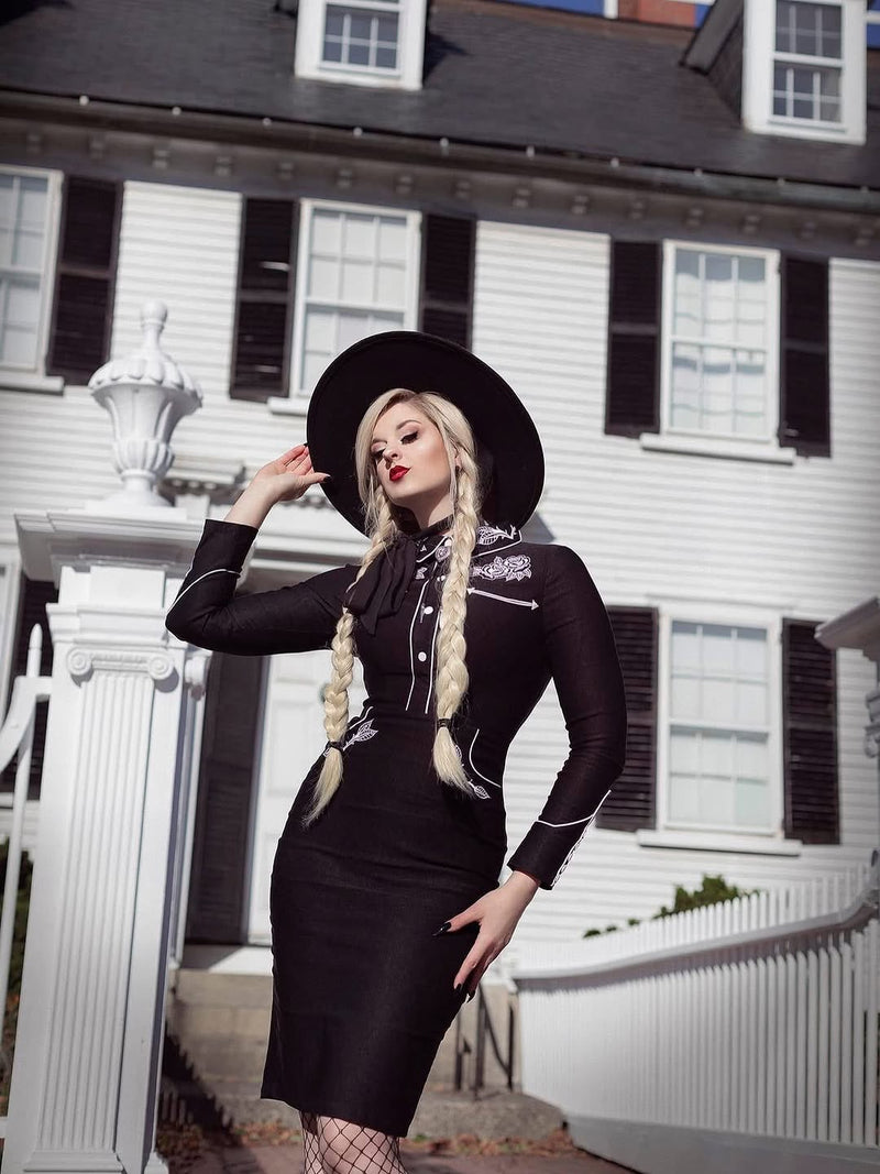 Woman in a black dress with white accents standing in front of a white house.