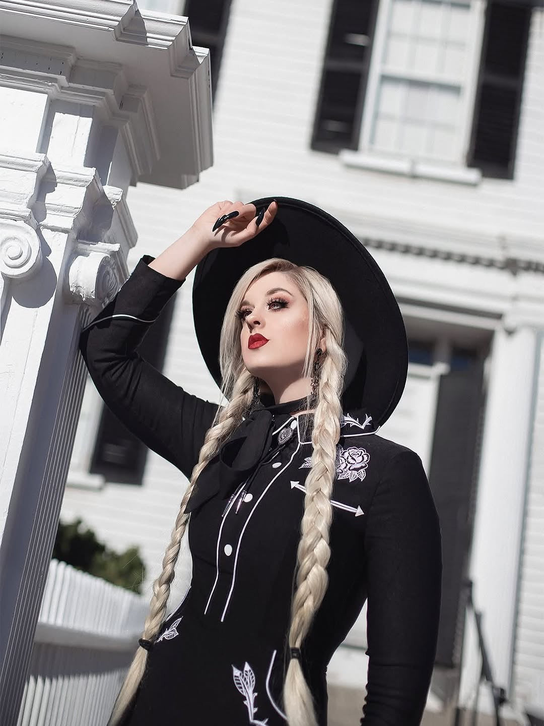 Woman in a black outfit with white embroidery standing in front of a white building.