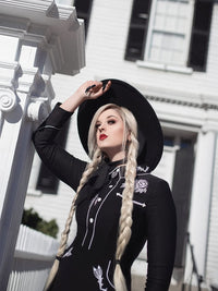 Woman in a black outfit with white embroidery standing in front of a white building.