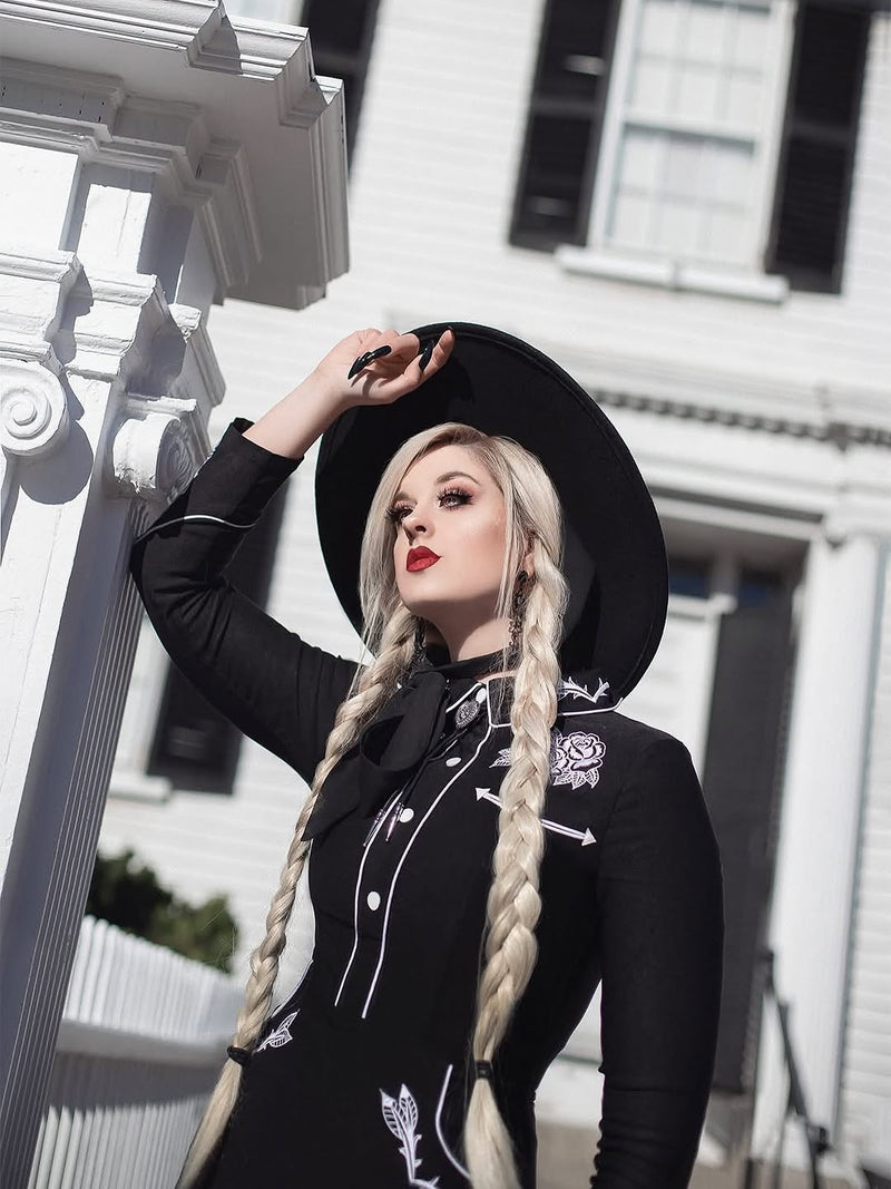 Woman in a black outfit with white embroidery standing in front of a white building.