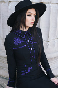 Sophisticated black and purple wiggle dress in stretchy bengaline, featuring long piped sleeves with decorative faux snap cuffs, front snaps for a seamless appearance, and elaborate rose and thorn embroidery across the collar, bust, hips, and cuffs, accented with white piping to complete the refined spring look.