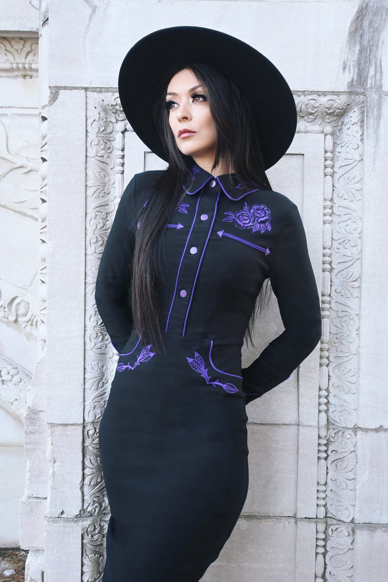 Form-fitting June Dress in black and purple bengaline, combining long piped sleeves, faux snap cuffs, and fixed front snaps with exquisite rose and thorn embroidery at the collar, bust, hips, and cuffs, enhanced with subtle white piping for an elegant and striking springtime outfit.