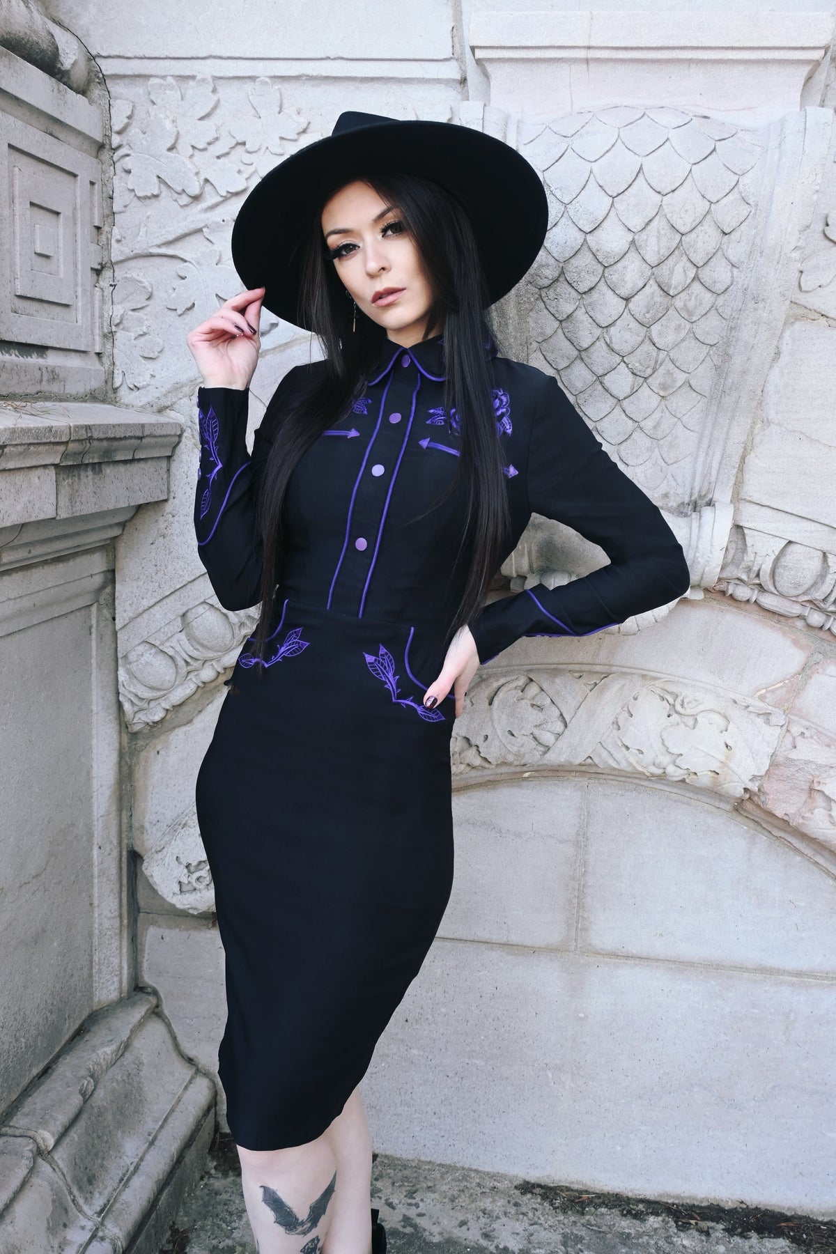 Stretchy black and purple June Dress with long piped sleeves, faux snap cuffs, and front snaps that maintain a seamless finish, adorned with detailed rose and thorn embroidery on the collar, bust, hips, and cuffs, and highlighted by white piping for a stylish and sophisticated spring wiggle dress.