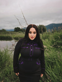 Sophisticated black and purple wiggle dress in stretchy bengaline, featuring long piped sleeves with decorative faux snap cuffs, front snaps for a seamless appearance, and elaborate rose and thorn embroidery across the collar, bust, hips, and cuffs, accented with white piping to complete the refined spring look.