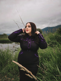 Sophisticated black and purple wiggle dress in stretchy bengaline, featuring long piped sleeves with decorative faux snap cuffs, front snaps for a seamless appearance, and elaborate rose and thorn embroidery across the collar, bust, hips, and cuffs, accented with white piping to complete the refined spring look.