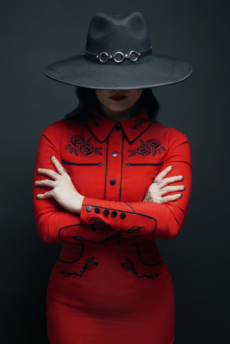 The June Dress in vibrant red channels June Carter’s iconic country style with a modern gothic twist. Featuring floral rose and thorn embroidery across the collar, cuffs, bust, and hips, along with shiny pleather piping and soft stretch bengaline fabric, it offers a flattering, body-contouring silhouette ideal for vintage and rockabilly fashion lovers.