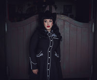 Black and white June Dress featuring a feminine skater skirt design, intricate rose and thorn embroidery along the collar, bust, hips, and cuffs, elegant white piping accents, long piped sleeves with faux snap cuffs, and deep, practical pockets, combining whimsical charm, chic detailing, and everyday versatility.