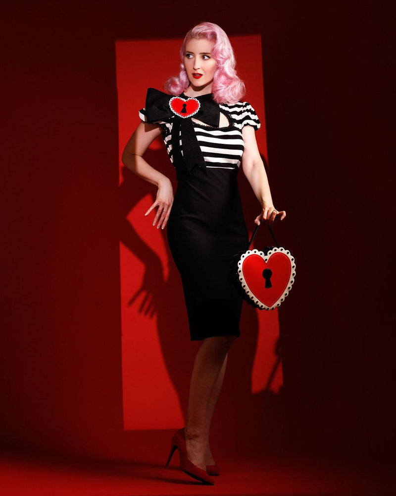 The Molly Keyhole Dress by Jessica Louise is a stretchy, form-fitting bengaline dress that beautifully accentuates feminine curves. Designed with a flattering high waistline, puff sleeves, and a ruffled skirt hem, this piece combines playful charm with vintage-inspired elegance. The signature keyhole cutout at the bust adds a flirty touch, while Jessica’s signature Heart Bow detail completes the look with whimsical flair. Perfect for alternative fashion lovers.