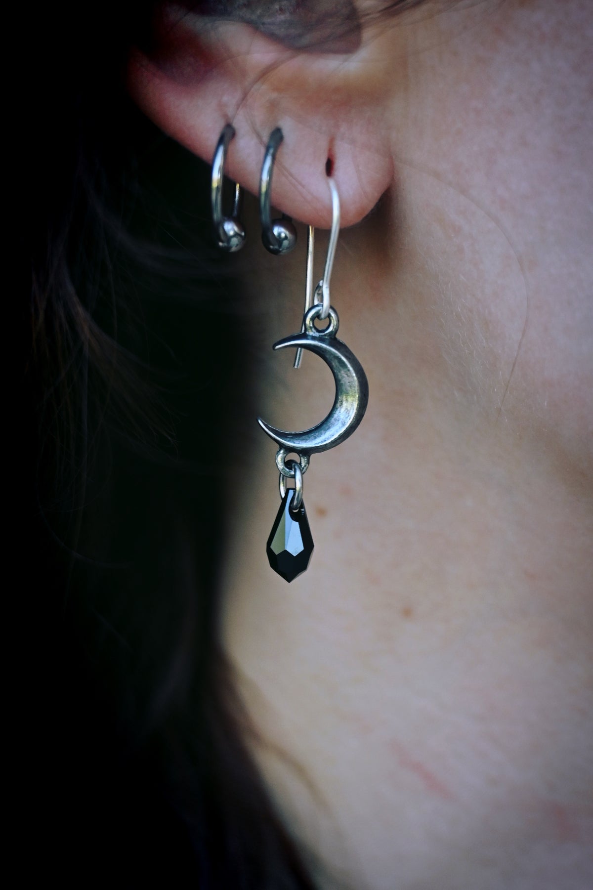Sleek and dramatic moon-drop earrings featuring a handcrafted pewter crescent and a dark crystal pendant, evoking night-time enchantment and resilience—designed for stylish wear while being hypoallergenic and tarnish-resistant.