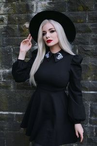 The Moon Flower Dress in deep black combines celestial charm and timeless style with its white embroidered moon and flower detailing on a wide collar, complemented by dramatic puff shoulders and long bishop sleeves in thick ponte material that provides warmth and flexibility.