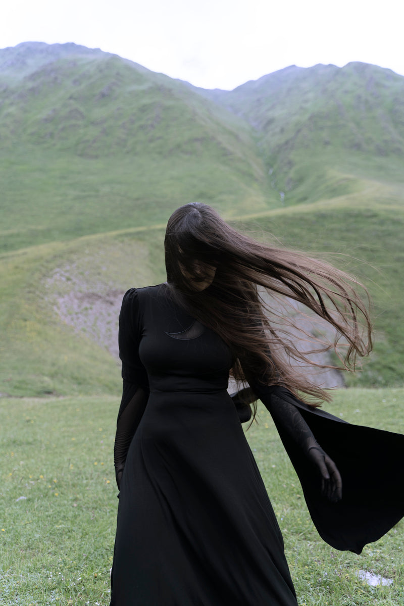 Moonveil Dress in black, featuring soft high-stretch polyester, sleek mock neck, sheer mesh crescent moon chest detail, long flowing cape sleeves parted at the elbows, and a mystical night-inspired design ideal for gothic or ethereal fashion lovers.
